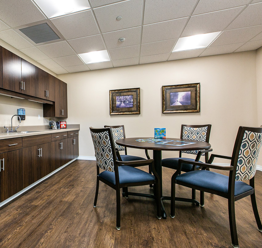 Hawkeye Care Center kitchen area with a round table with an unfinished puzzle on top, 4 dining chairs, and a counter with cabinets and sink