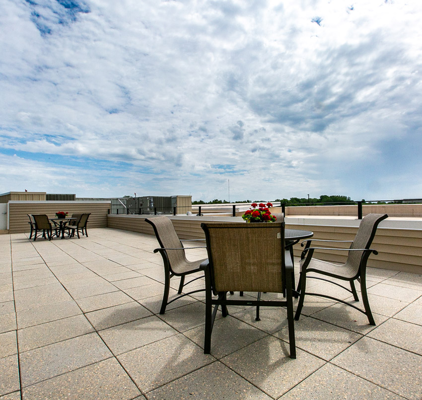 Hawkeye Care Center outdoor seating area on a balcony with two metal patio tables, each with 4 chairs, and red flowers on the center