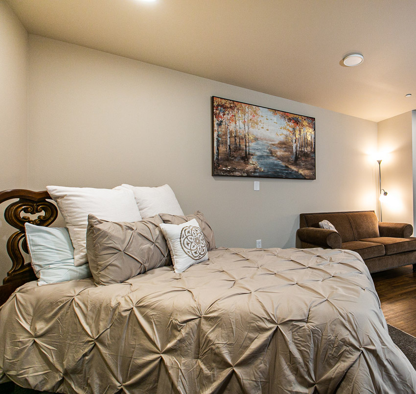 Hawkeye Care Center bedroom with a queen sized bed made up with beige comforter and several pillows, and a brown couch.