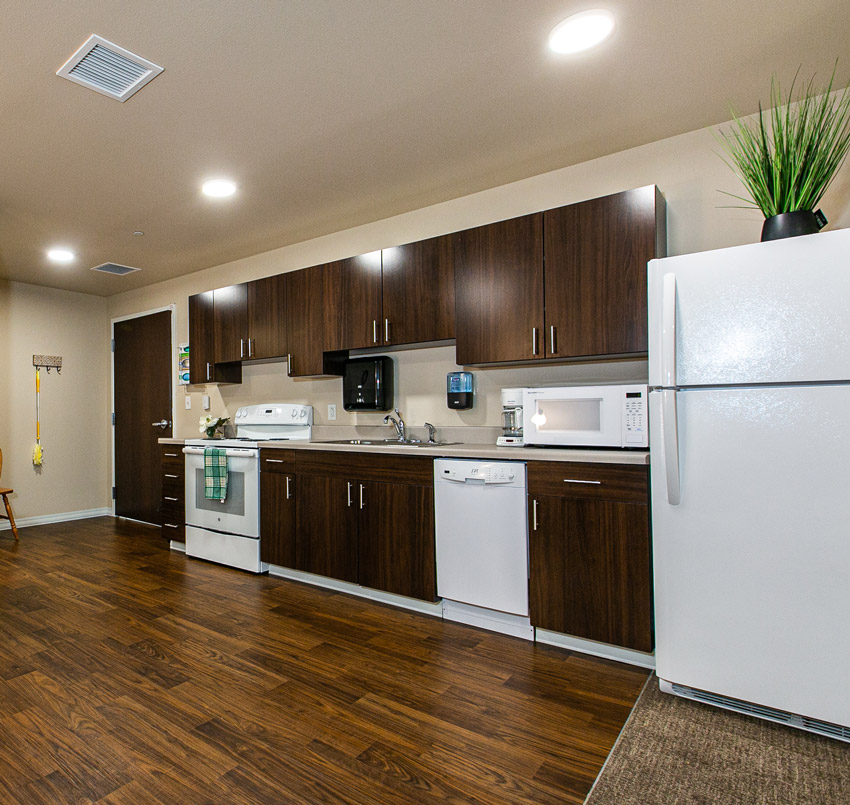 Hawkeye Care Center in-room kitchen area with dark wood cabinets and white appliances.