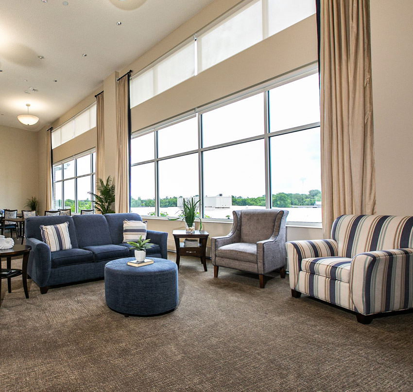 Hawkeye Care Center sitting area, with a blue couch, gray arm chair, blue and white striped arm chair, and floor-to-ceiling windows