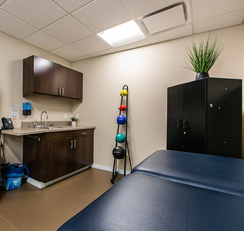 Hawkeye Care Center physical therapy room with a dark blue medical bed, dark wood cabinets, medicine balls, and a counter with a sink